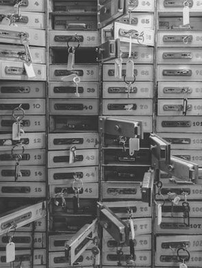 An array of numbered metal safety deposit boxes, many of which are open, each with a key and tag hanging from the lock.