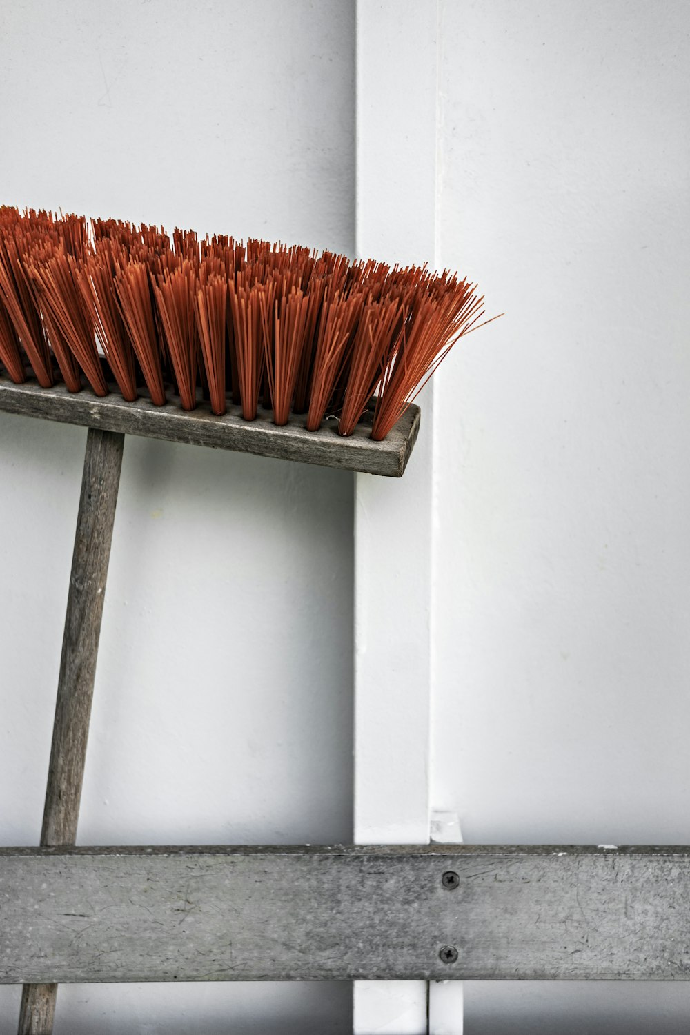 Balai-poussoir brun et orange à côté d’un mur blanc