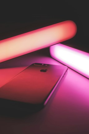 A sleek smartphone is placed on a flat surface surrounded by ambient, glowing pink and purple neon lights, creating a futuristic and modern atmosphere.