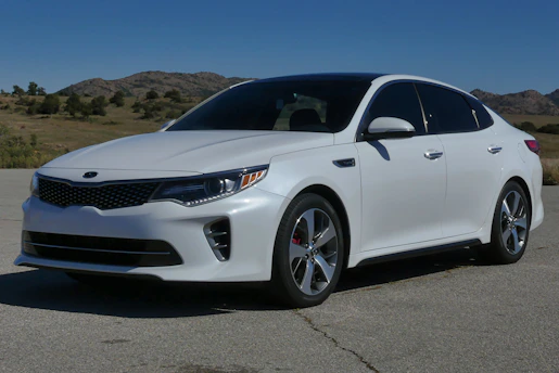 A sleek white sedan parked on a coastal road at sunset, highlighting its shiny exterior and inviting design.