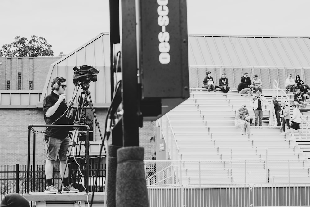 greyscale photography of man standing beside video camera