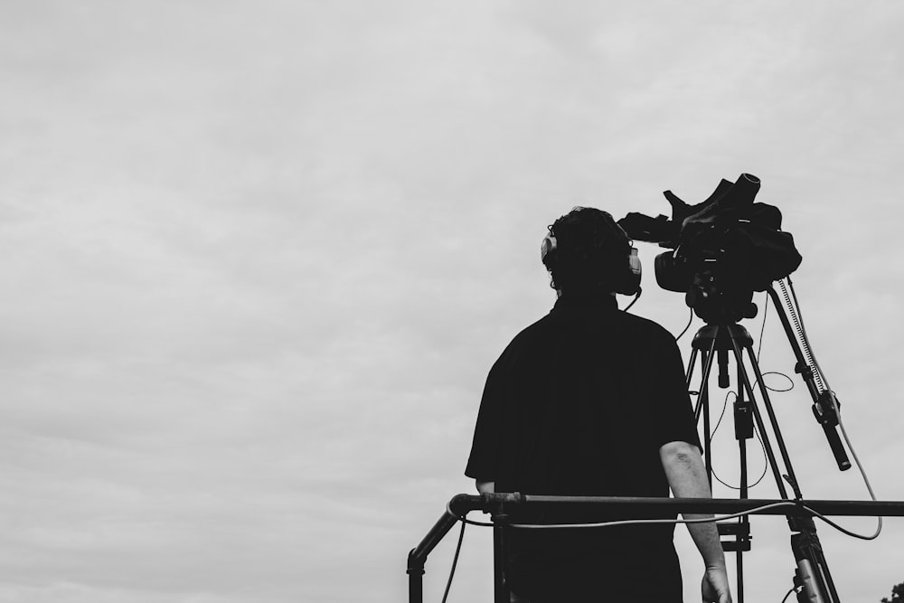 greyscale photography of man standing beside video camera