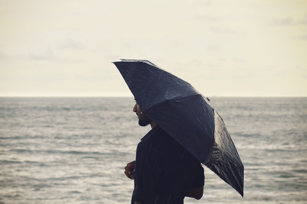 person holding umbrella near body of water