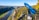 A scenic viewpoint overlooking a river canyon with a dense forest and rocky cliffs. A blue telescope labeled 'GALAXY' is mounted on a railing, offering a panoramic view of the landscape.