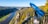 A scenic viewpoint overlooking a river canyon with a dense forest and rocky cliffs. A blue telescope labeled 'GALAXY' is mounted on a railing, offering a panoramic view of the landscape.