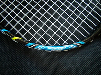 Close-up of a sleek black carbon fiber padel racket with subtle white accents on a dark background.