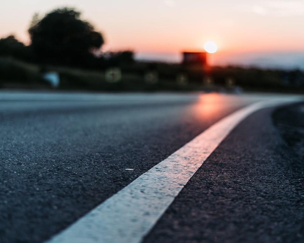 the sun is setting on a road with white lines