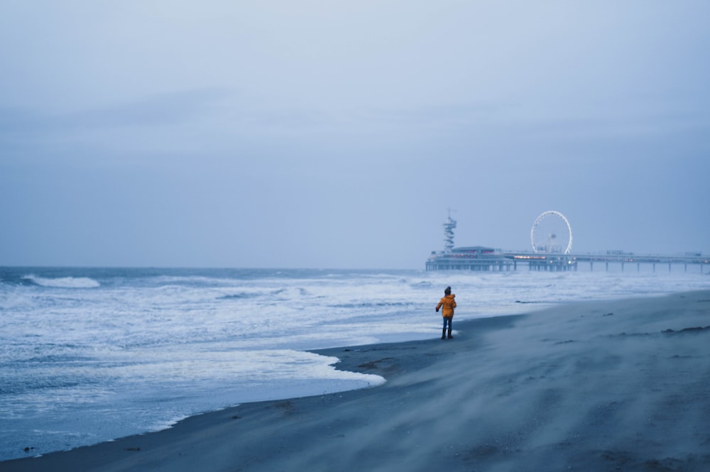 person wearin yellow jacket walking on seashore