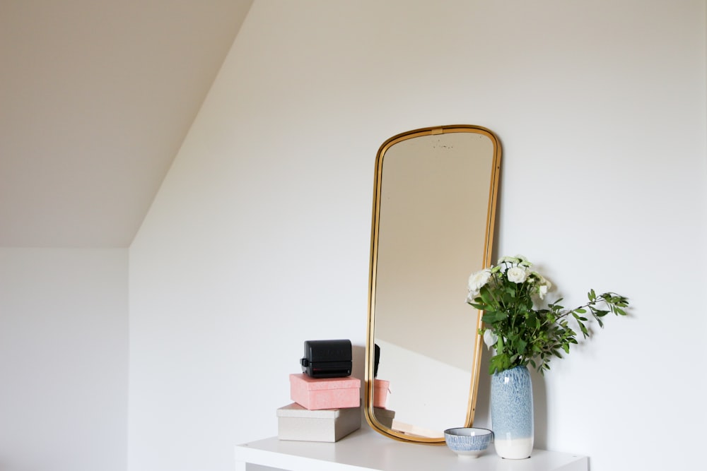 white petaled flowers in vase placed beside mirror