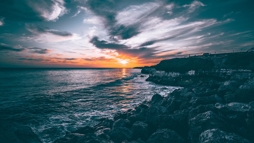 rocce grigie vicino all'oceano durante il tramonto