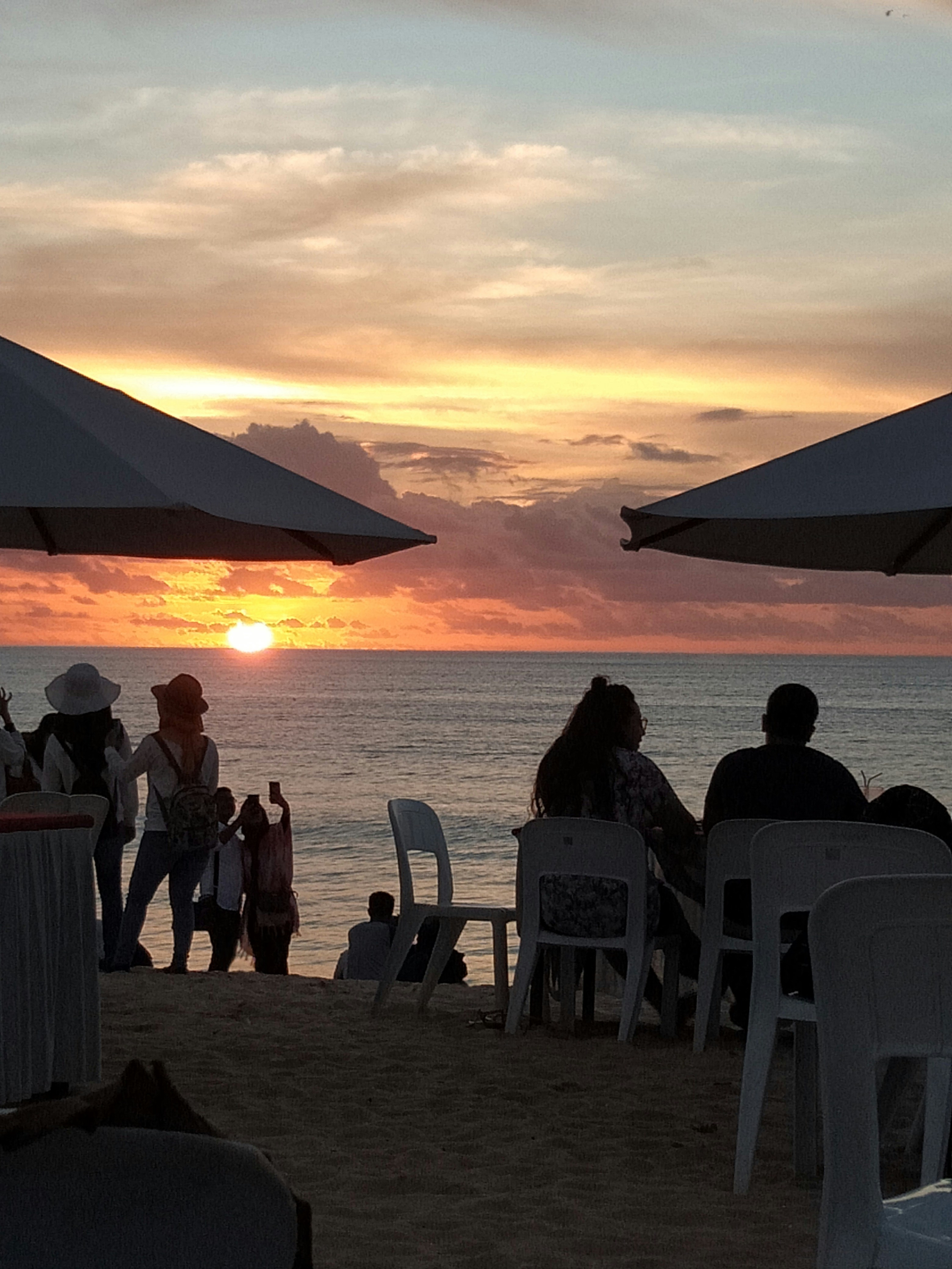 people on shore beside umbrella near sea during golden hour