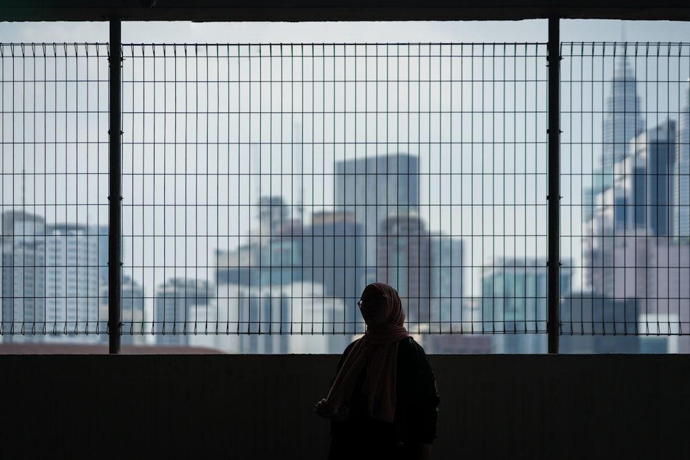 standing woman in brown hijab beside wall with grill