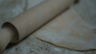A rustic rolling pin resting on a floured wooden countertop.