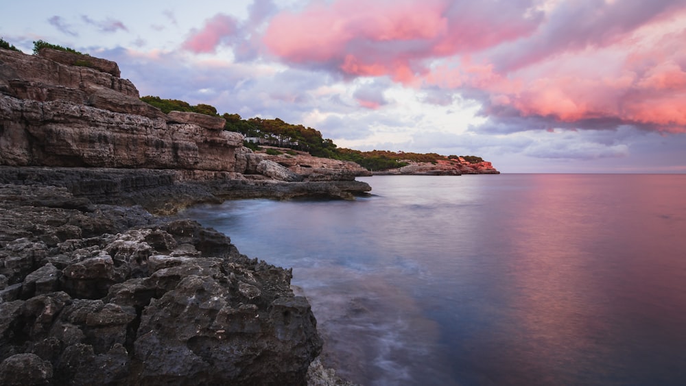 a pink and purple sky over a rocky shoreline