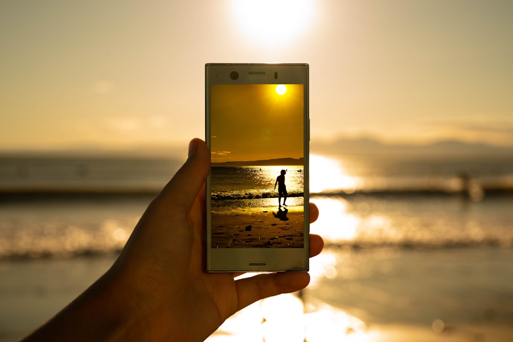 person holding phone showing person on seashore