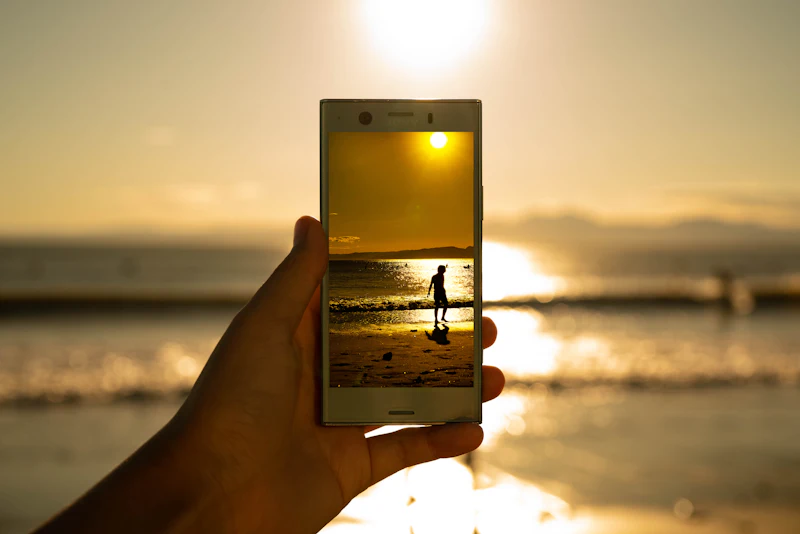 Hand holding a smartphone up to a golden beach sunset, the moment a travel eSIM should connect