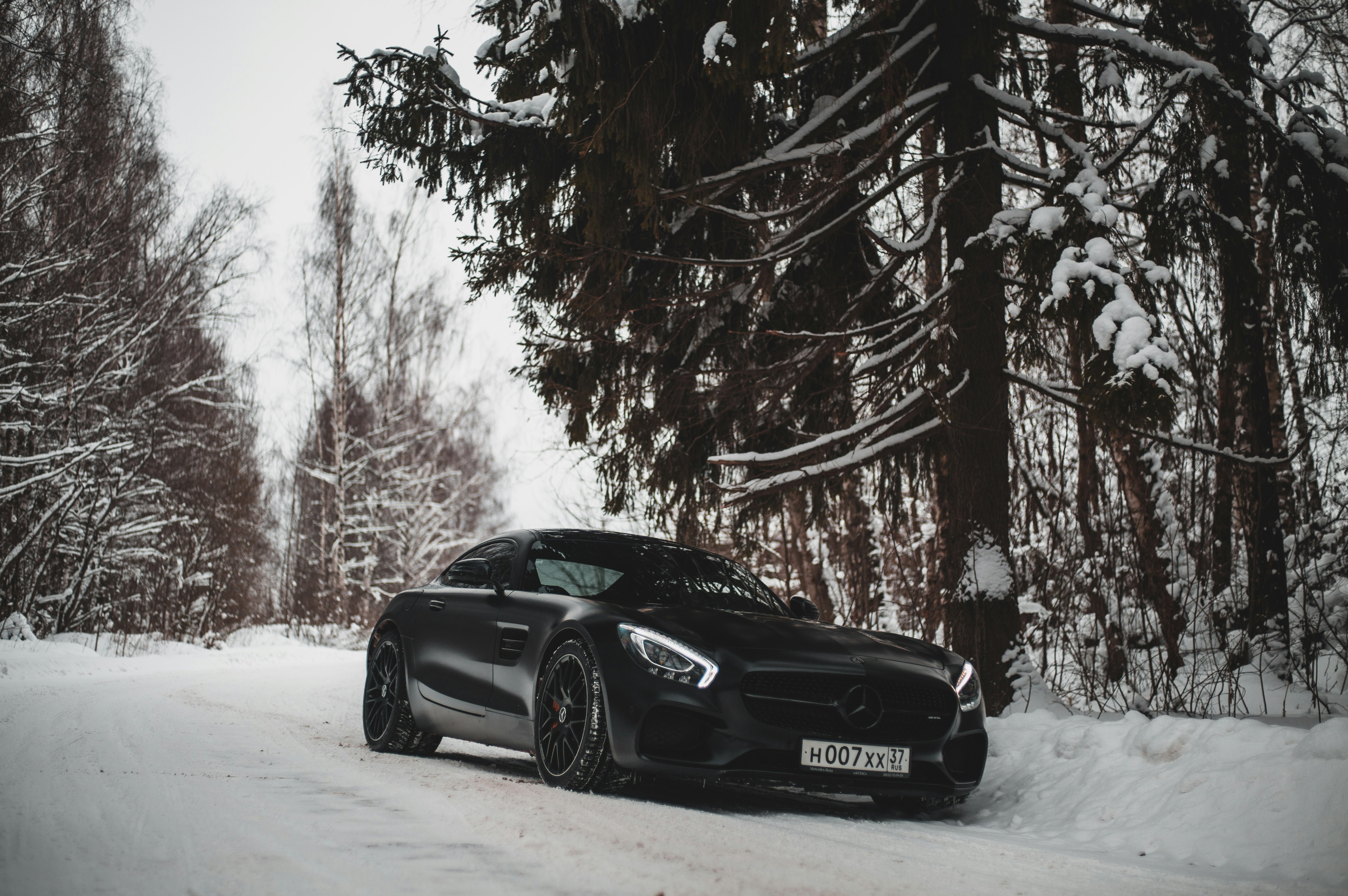black sports car parked on snow road beside trees