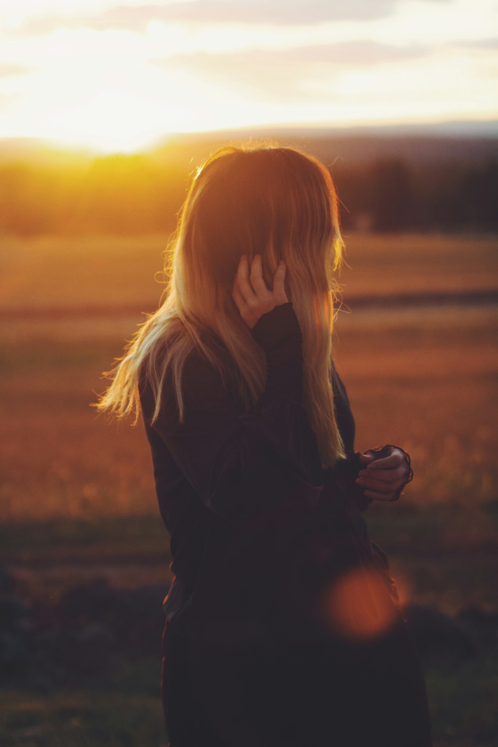 woman wearing long-sleeved shirt touching her hair while standing and glancing right side