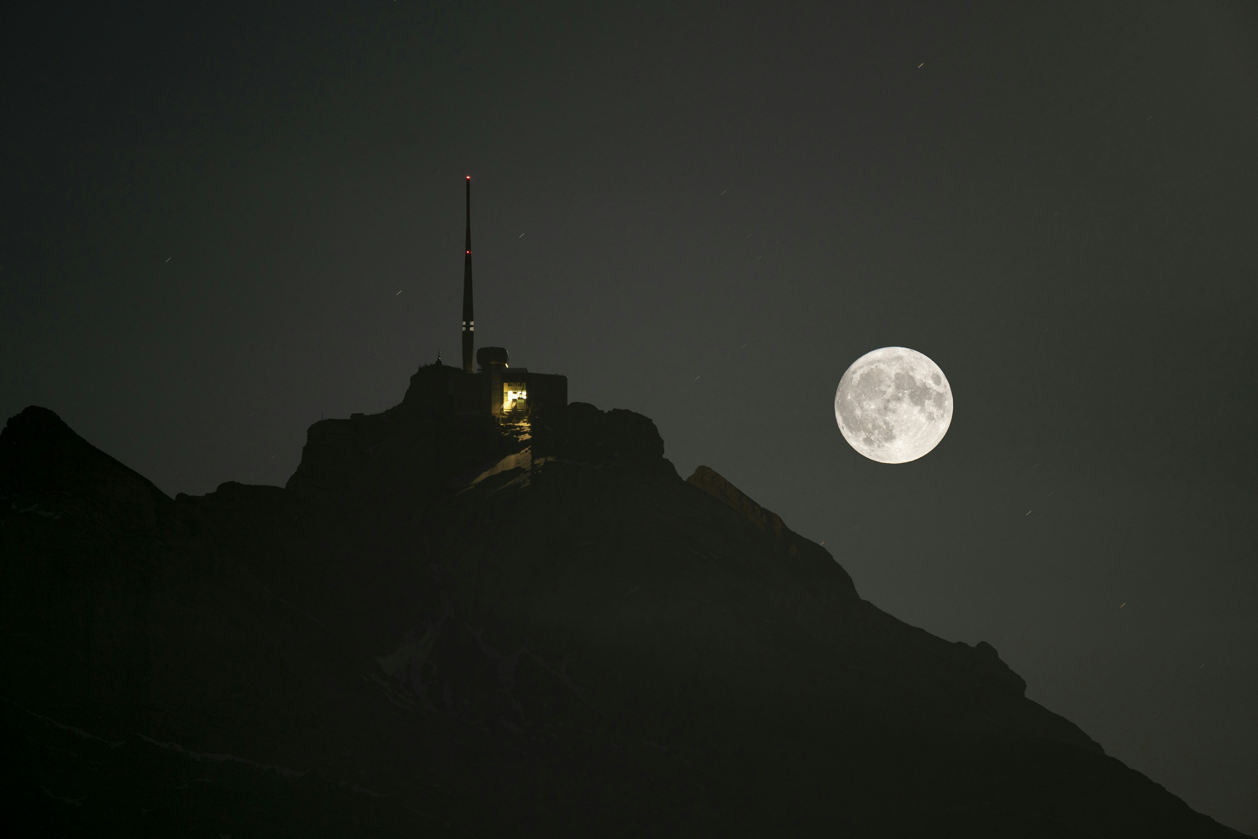 a full moon rising over a mountain with a radio tower
