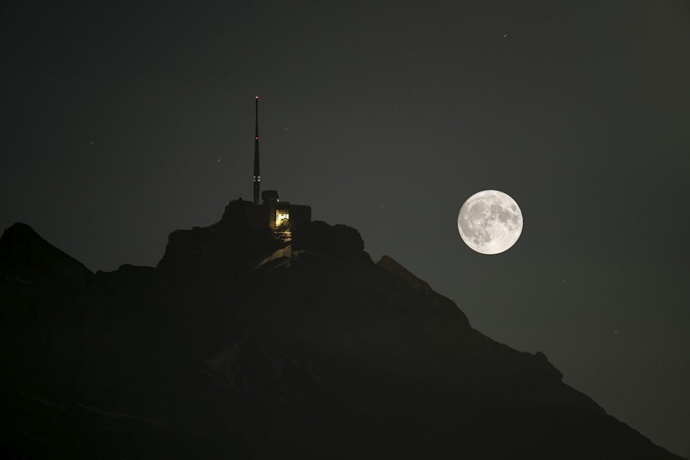 a full moon rising over a mountain with a radio tower