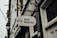 A metal sign with the words 'Bike Rental' hangs from a decorative bracket on a building. The sign includes icons of a bicycle and navigation symbols. The building has a white door and the number '135' visible. The atmosphere appears overcast, contributing to a muted tone.