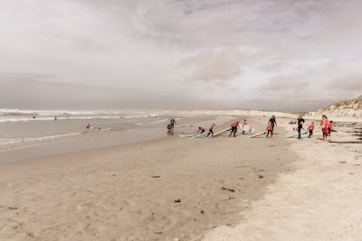 A group of surfers laughing and preparing their boards on the sandy beach before heading out.