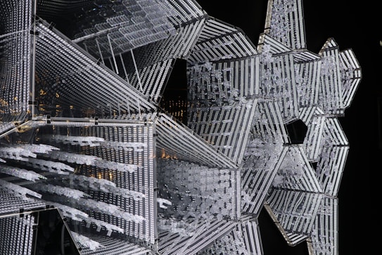An intricate geometric structure composed of illuminated patterns and interlocking shapes with a reflective surface. The design features a combination of linear and star-like formations, creating a complex visual effect.