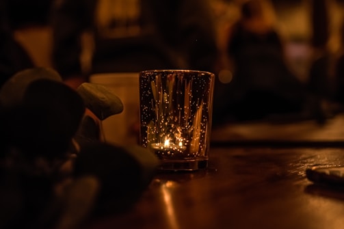 An atmospheric shot of a candle lit in a cozy home setting, casting warm light on natural decor elements.