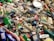 A pile of discarded plastic bottles and containers, some with colorful labels, mixed with other waste and debris. The items are scattered haphazardly, indicating pollution and environmental neglect.
