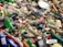 A pile of discarded plastic bottles and containers, some with colorful labels, mixed with other waste and debris. The items are scattered haphazardly, indicating pollution and environmental neglect.