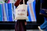 A person is walking while carrying a canvas tote bag with a design promoting diversity, reading 'The Power of Different' along with images of various dogs. The background features a vibrant, abstract display with vertical streaks of color.