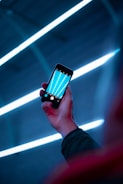 A glowing smartphone displaying a futuristic app interface with cyan and blue neon highlights