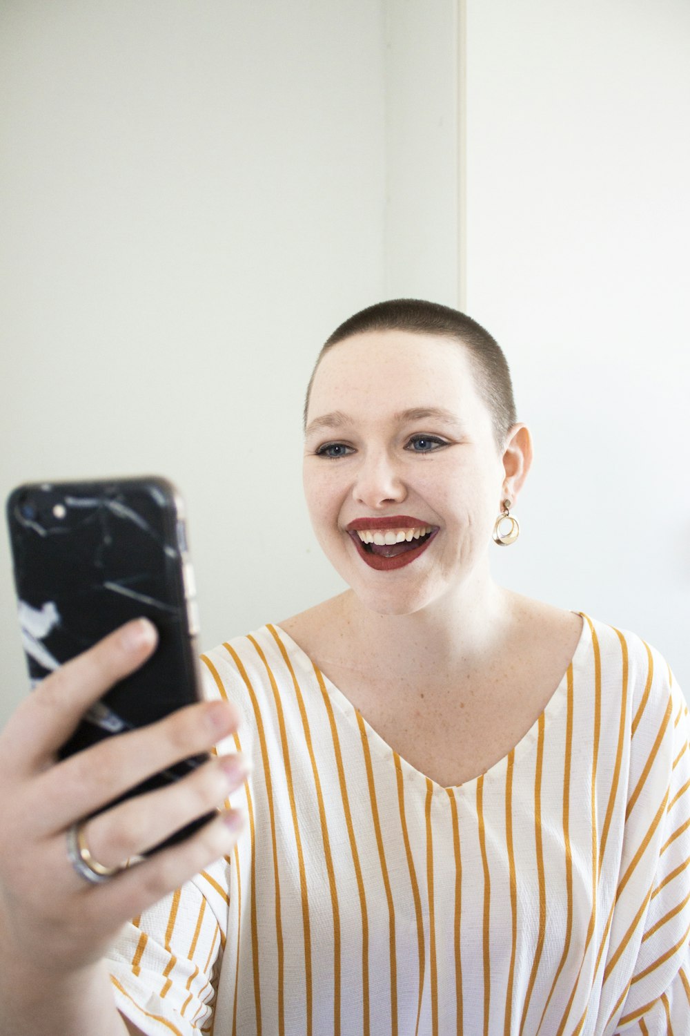 woman in white and gold striped top holding phone