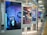 A series of large digital displays are positioned in a subway or transit station setting, each showing different artistic portraits. The nearest display features an image of a woman in a room with blue lighting and decorative items like a mobile and wall art. The scene is modern and artistic, with a focus on individual expressions and creativity.