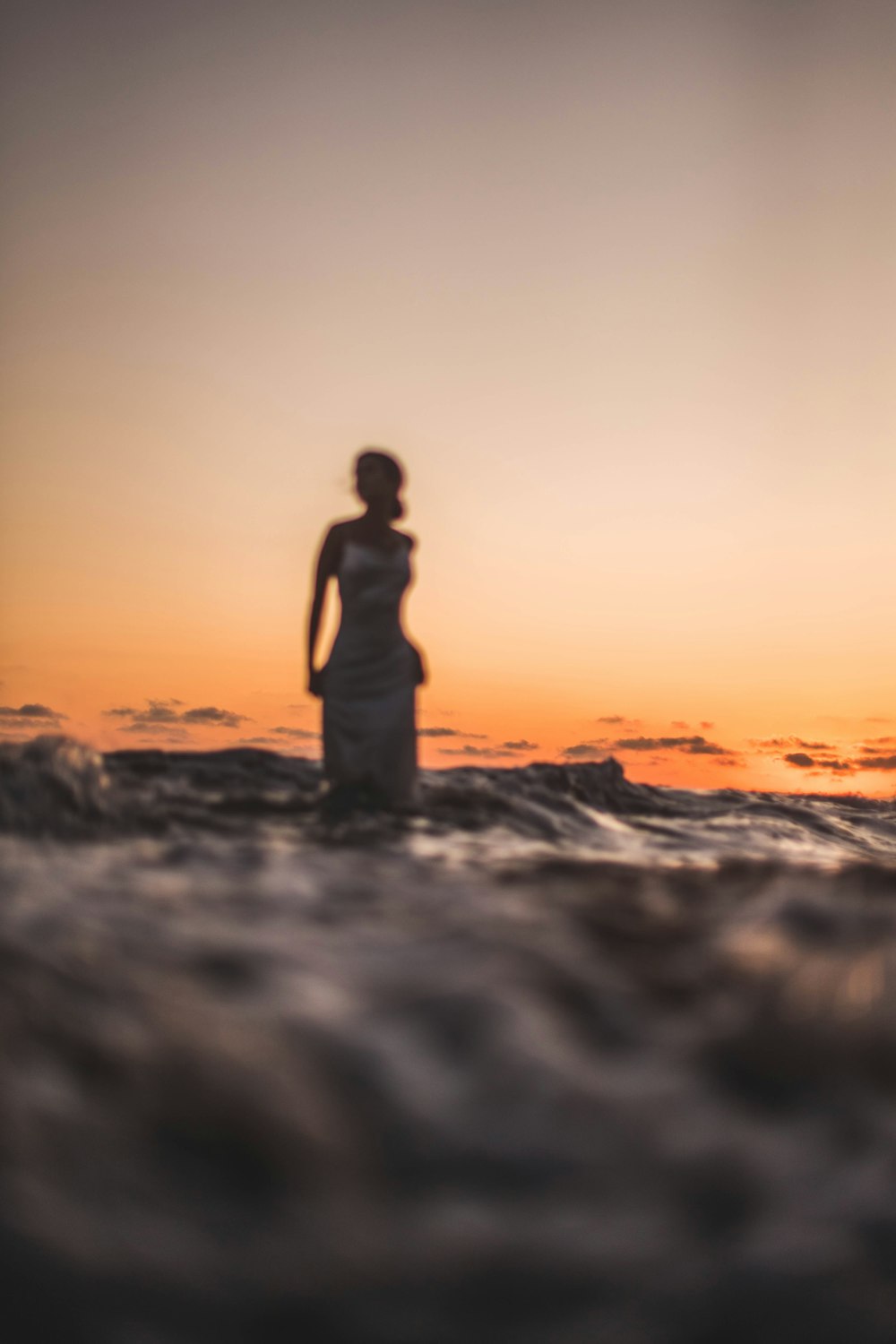 a woman standing in the ocean at sunset