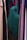 A person wearing a dark green hijab is standing among rows of colorful hanging fabrics. The fabrics include shades of purple, pink, tan, and green, creating a diverse and vibrant backdrop.