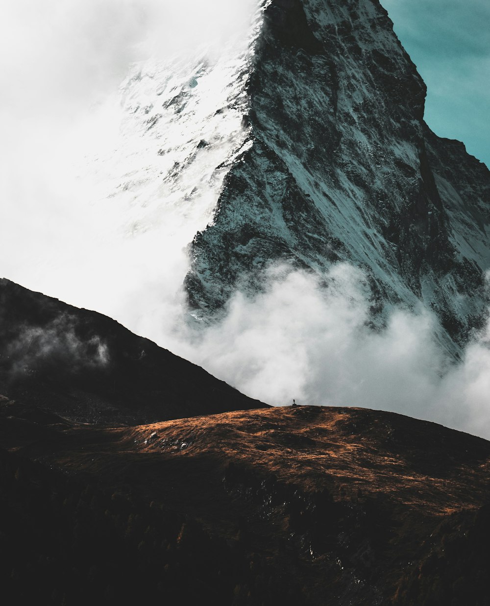 a mountain with clouds and a person standing on top of it