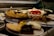 A display case filled with various types of cakes and desserts, including a caramel swirl cake, a strawberry-topped pastry, and a dessert with nuts. The arrangement is behind glass, highlighting the vibrant colors and textures of the treats.