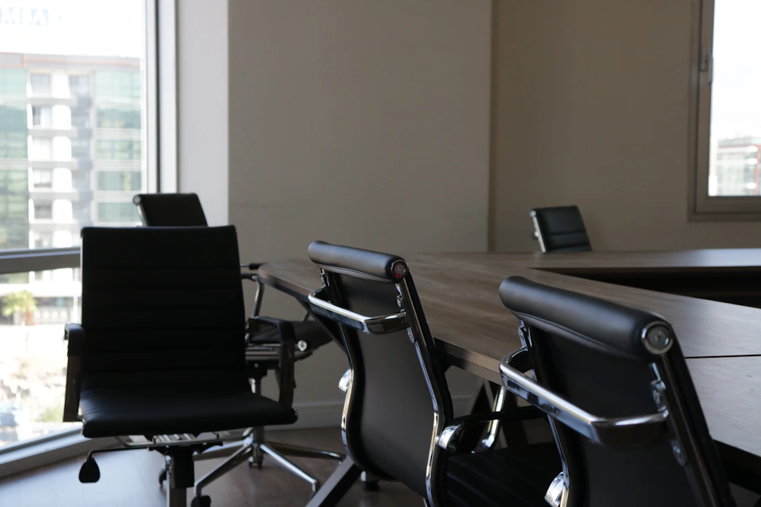 An empty boardroom with leather chairs and a long table by a window