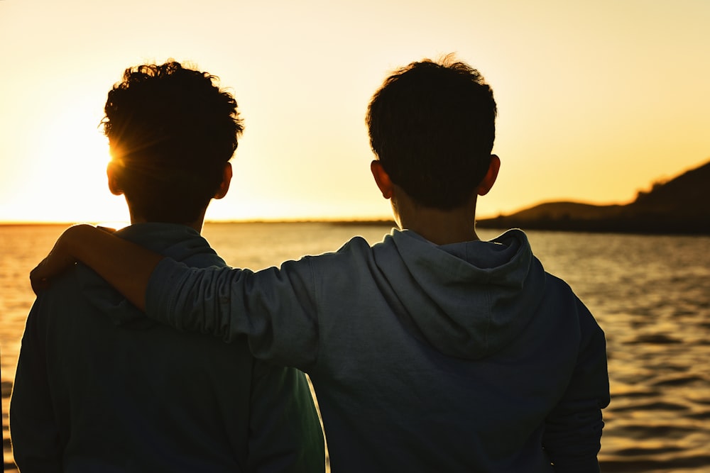 close-up photography of two men facing on seashore during sunset