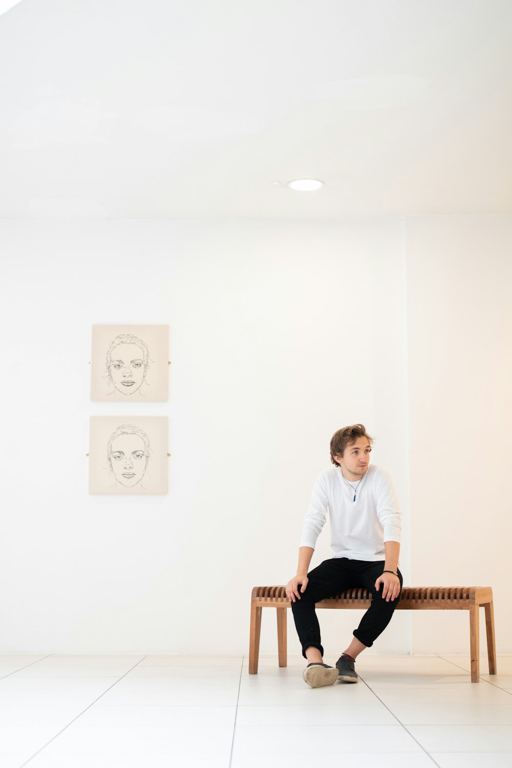 man in white shirt sitting on bench beside portraits