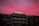 A building with multiple stories features the word 'RICHMAN' in illuminated letters on its rooftop. The sky above is a blend of vibrant pink and purple hues, suggesting either sunrise or sunset, casting a dramatic backdrop.