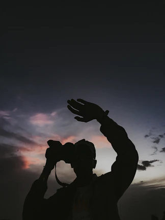 A candid photo of a smiling person holding a camera against a sunset backdrop.