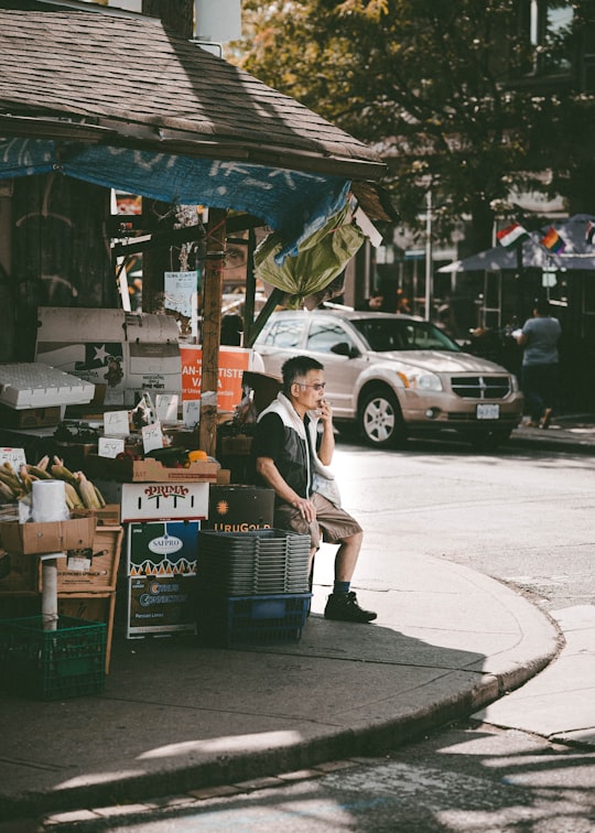 man sitting on chair near parked vehicle in Kensington Market Canada