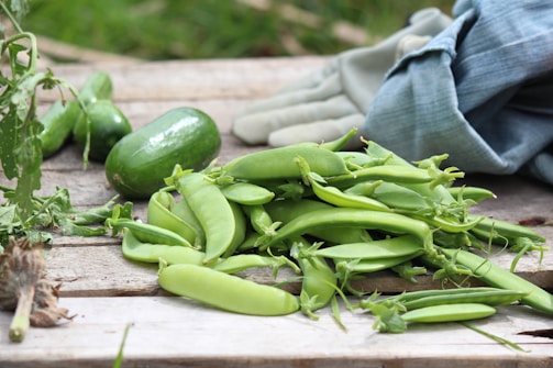 Set of colorful gardening gloves placed next to freshly harvested vegetables.
