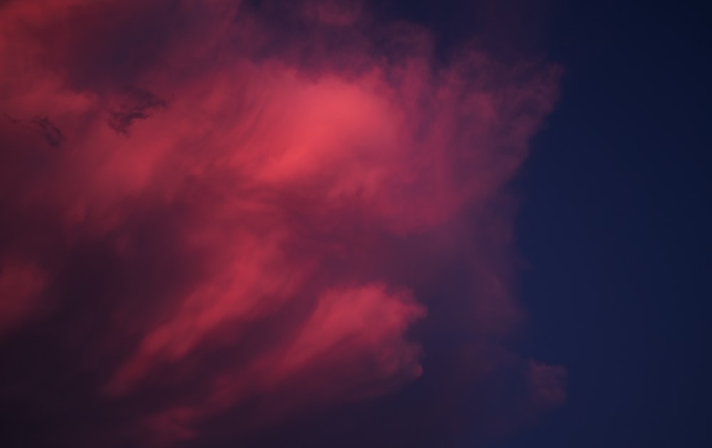 a red cloud in a blue sky with a plane in the distance