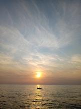 A serene sunset over a calm ocean with a small boat approaching the shore.