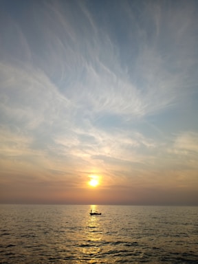 A serene sunset over a calm ocean with a small boat approaching the shore.