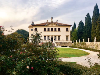 A stately villa with classic architecture surrounded by lush gardens at sunset.