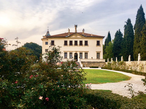 A stately villa with classic architecture surrounded by lush gardens at sunset.